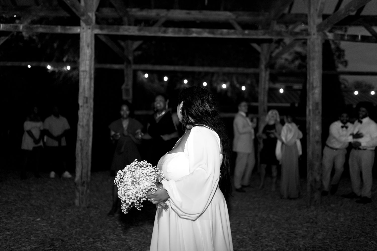 A group of people dancing and celebrating at night under string lights at an outdoor party.