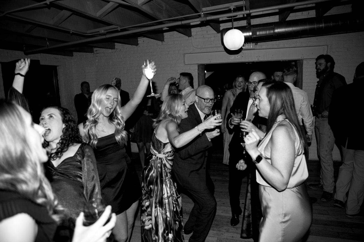 Black and white photo of party guests dancing enthusiastically at a lively indoor celebration.