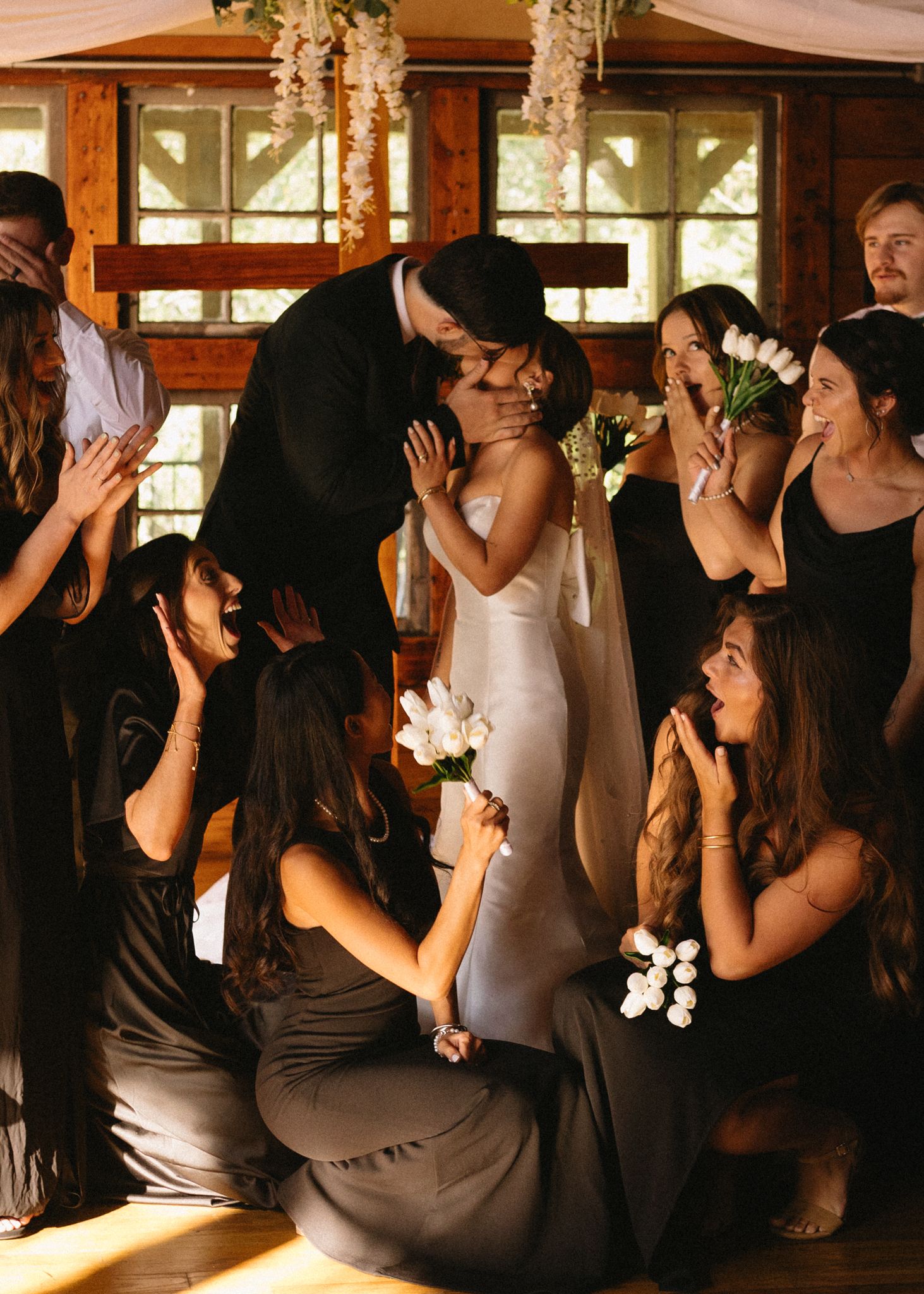 bride and groom surrounded by bridesmaids and groomsmen excited while sharing a kiss