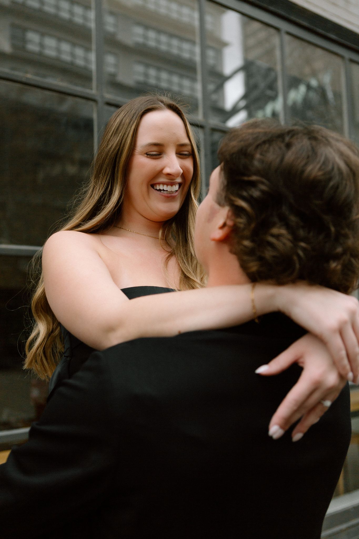 Engaged couple smiling and embracing, with the woman showing her engagement ring, captured in downtown Louisville