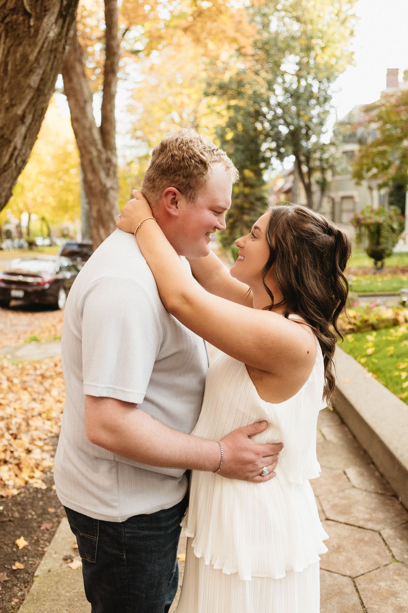 A romantic embrace on a fall day with golden leaves and historic buildings in the background.