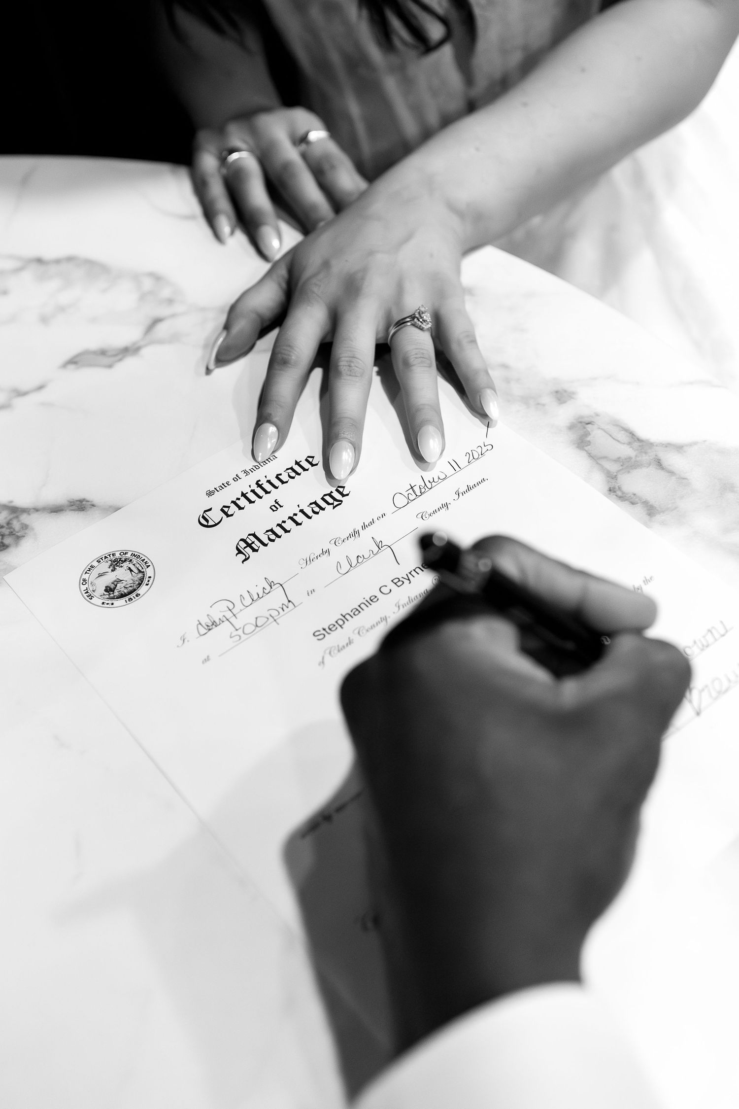 Close-up view of hands signing official wedding documents and certificates on white surface.