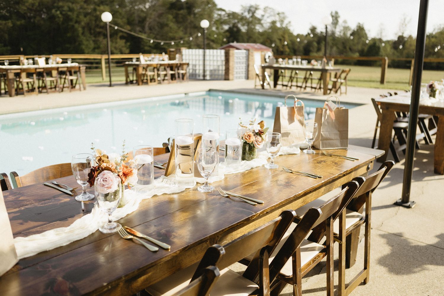 Long wooden tables set up outdoors for a wedding reception with pool visible in background.