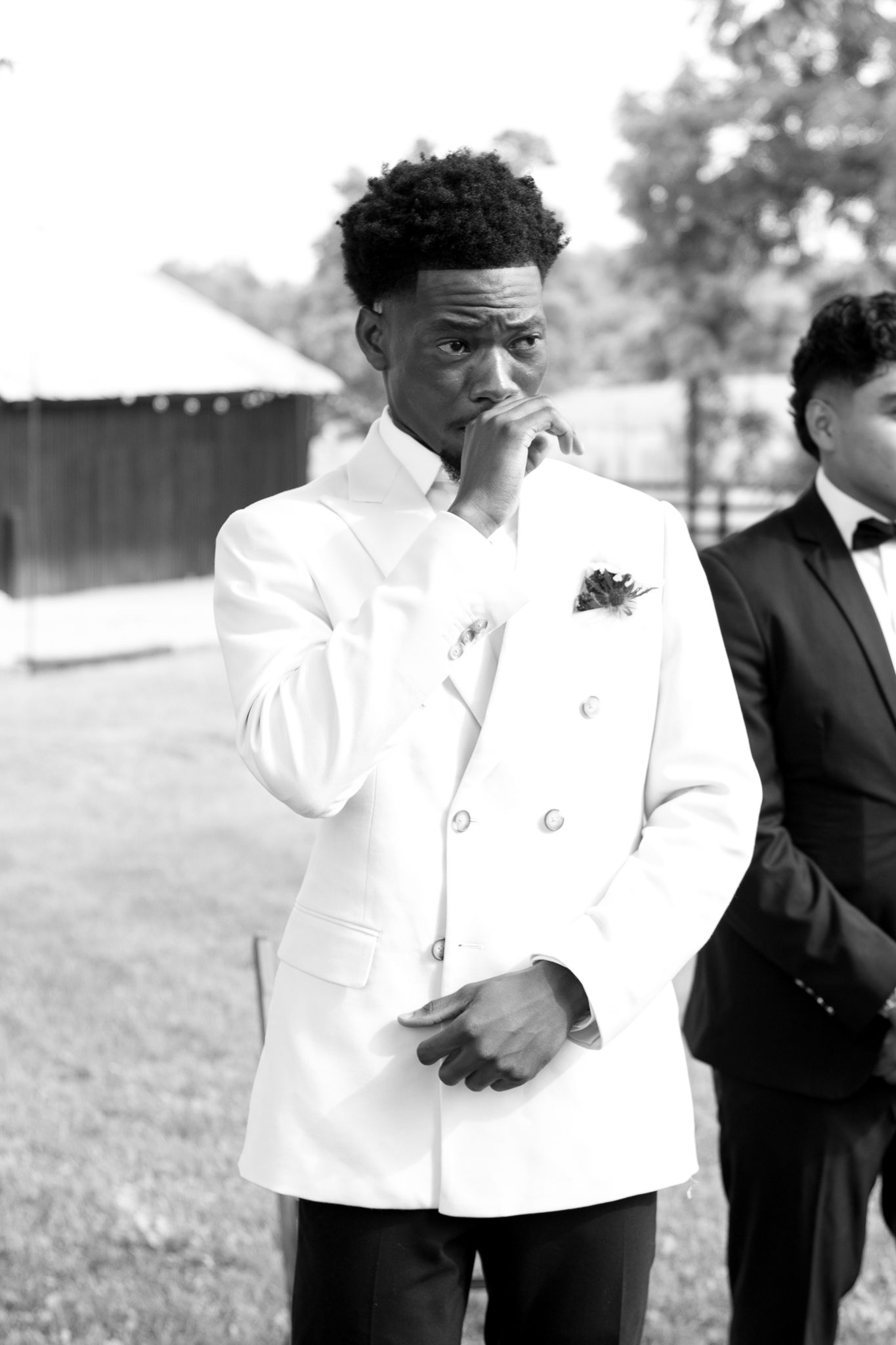 An emotional moment captured in black and white as a groom in a white tuxedo jacket shows his feelings.