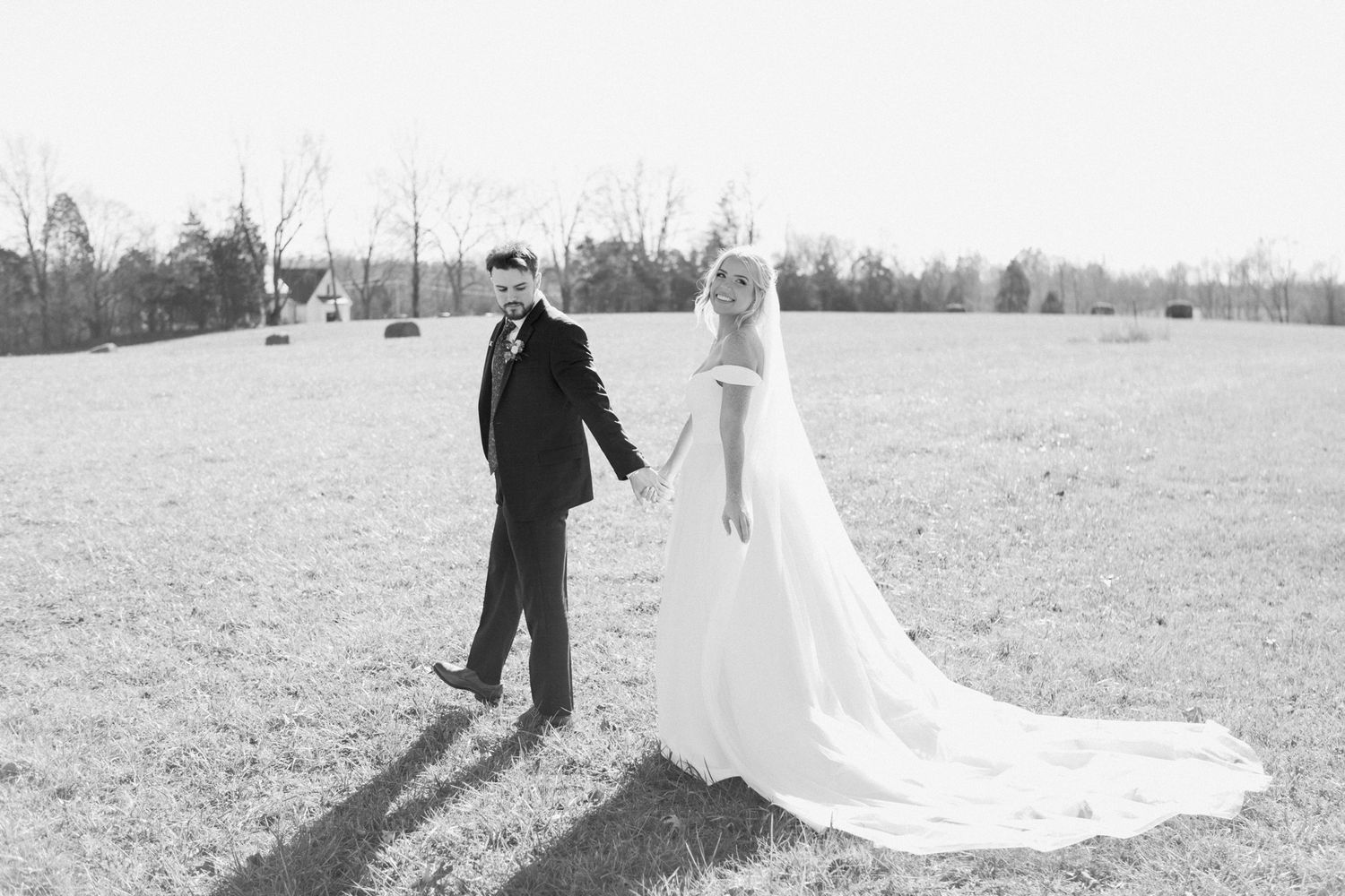Bride and groom walking through a sunny field at Silo Farms, captured in black and white. Photo by Joia Lyn, KY wedding