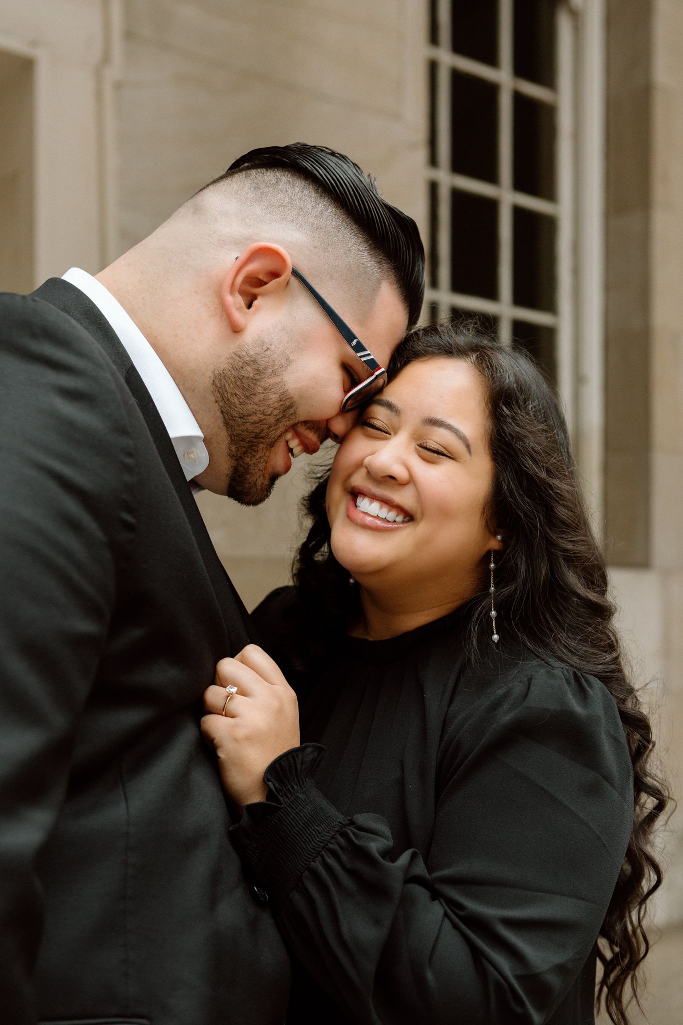 Engaged couple in downtown Louisville, with the woman smiling and showing her engagement ring while embracing her fiancé