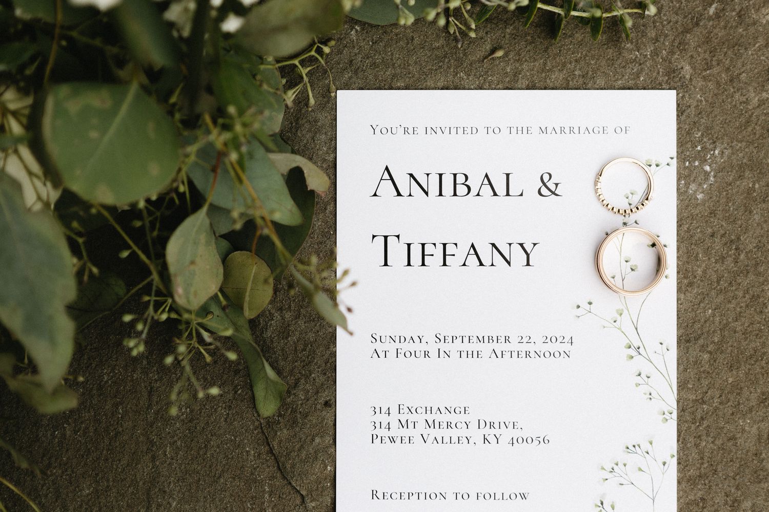 Wedding invitation with elegant typography and floral design for Anibal and Tiffany's celebration rests against greenery.
