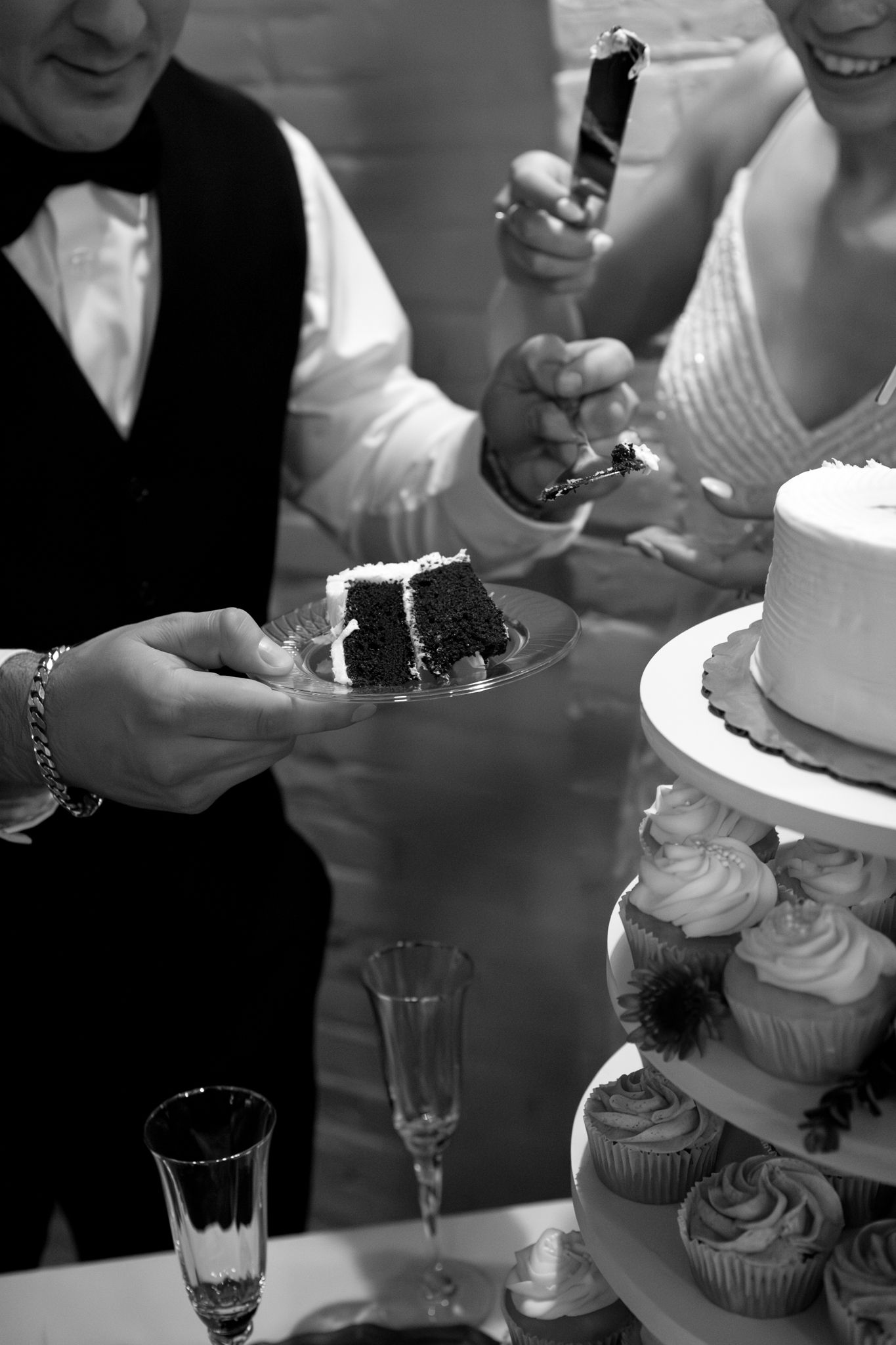 Black and white photo of wedding cake and cupcakes being served at a reception.