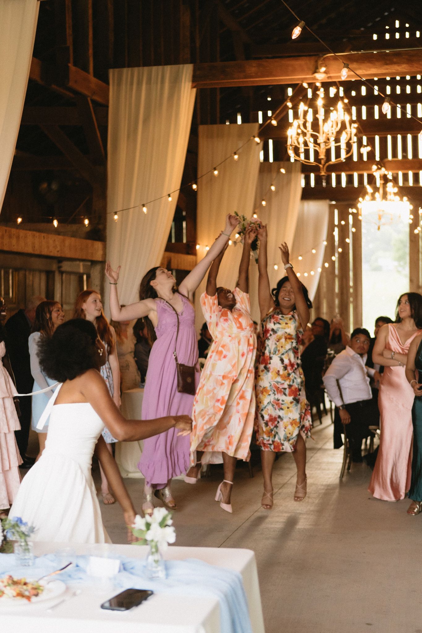 Wedding party dancing and celebrating in barn venue decorated with lights and white fabric.