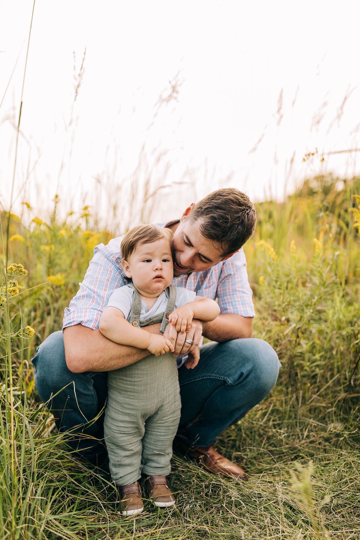 Dad and young son in a grassy field with wildflowers during the summertime.