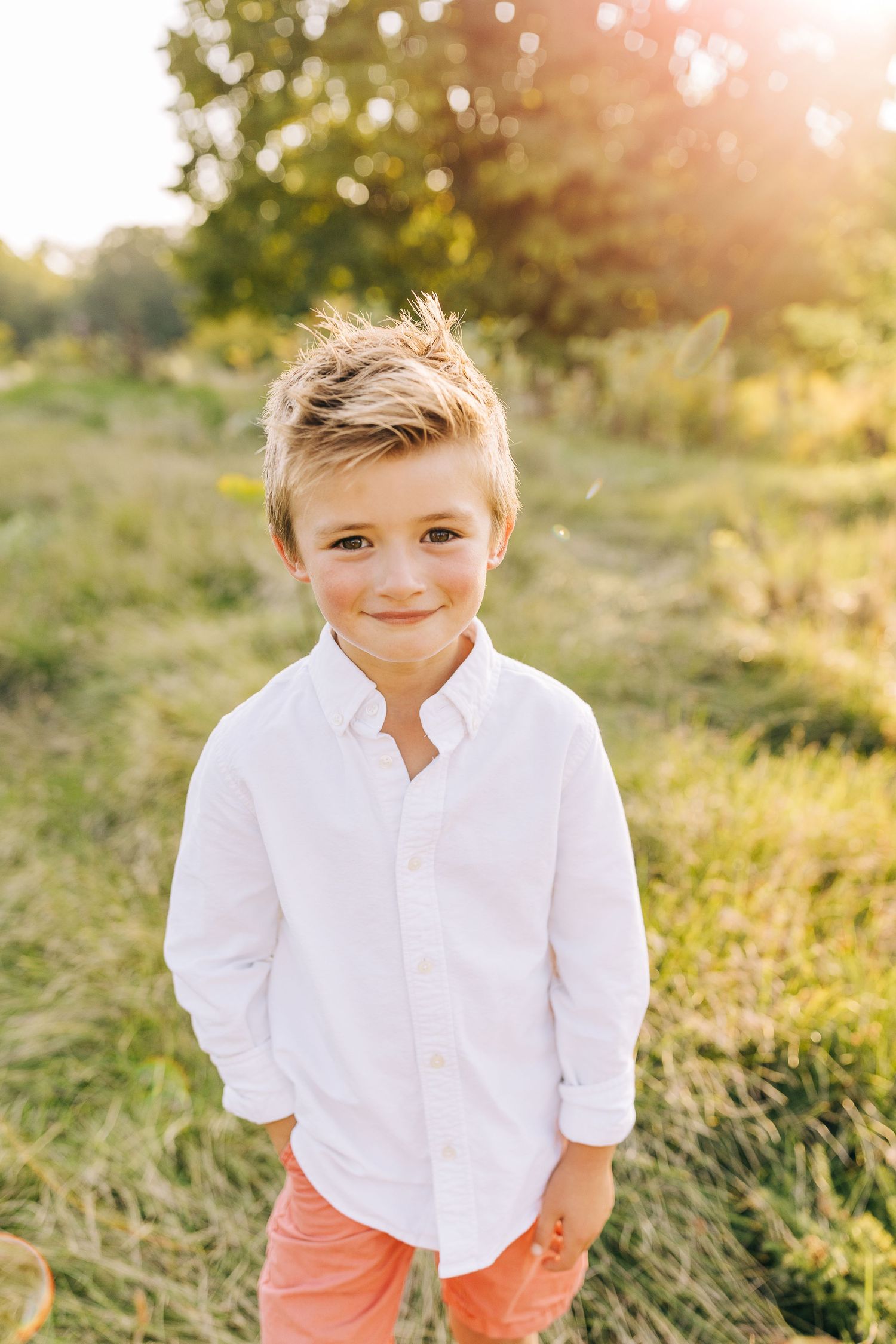 Young boy kneeling in grassy field at sunset in the summertime.