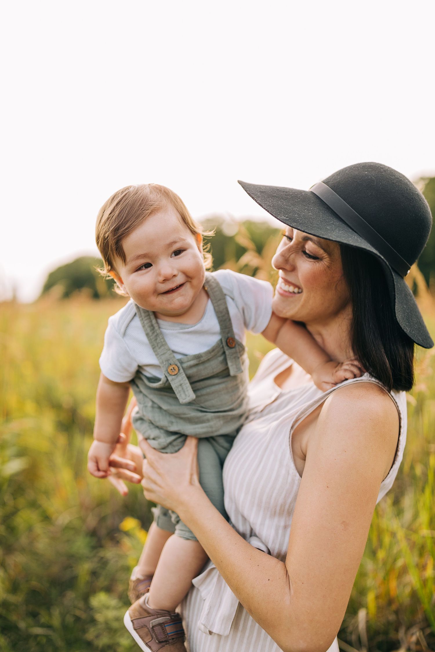 Mom holding her young son in a grassy field with wildflowers during the summertime at sunset.