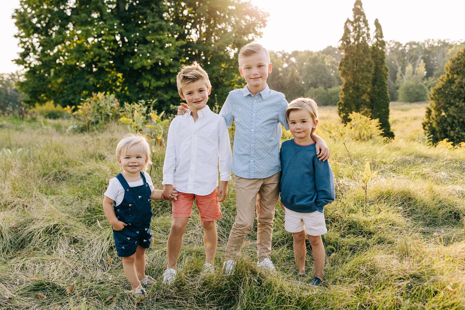 Young boys, brothers, standing in a grassy field at sunset.