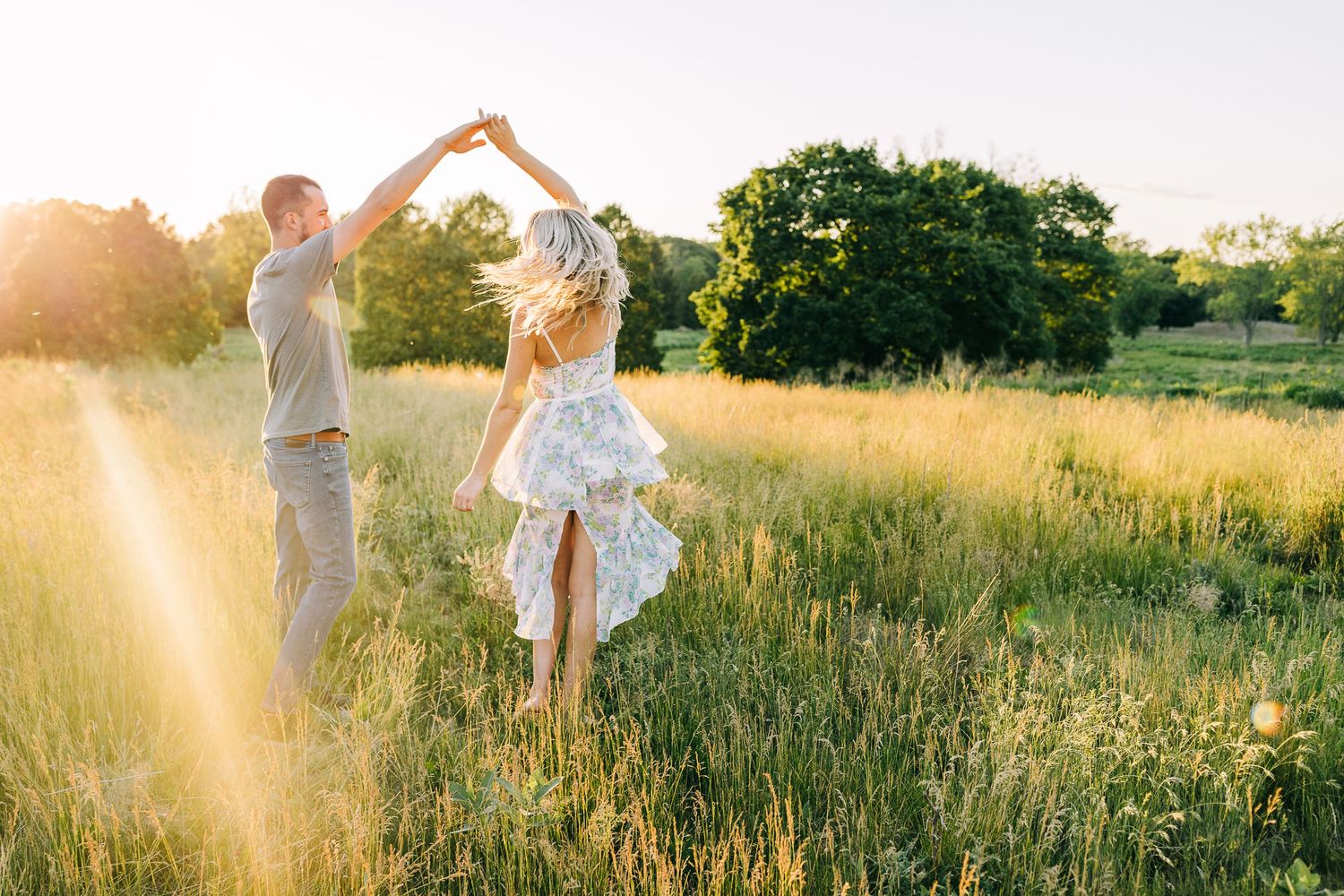 Engaged couple sharing a romantic moment while dancing in a wide open field during sunset.
