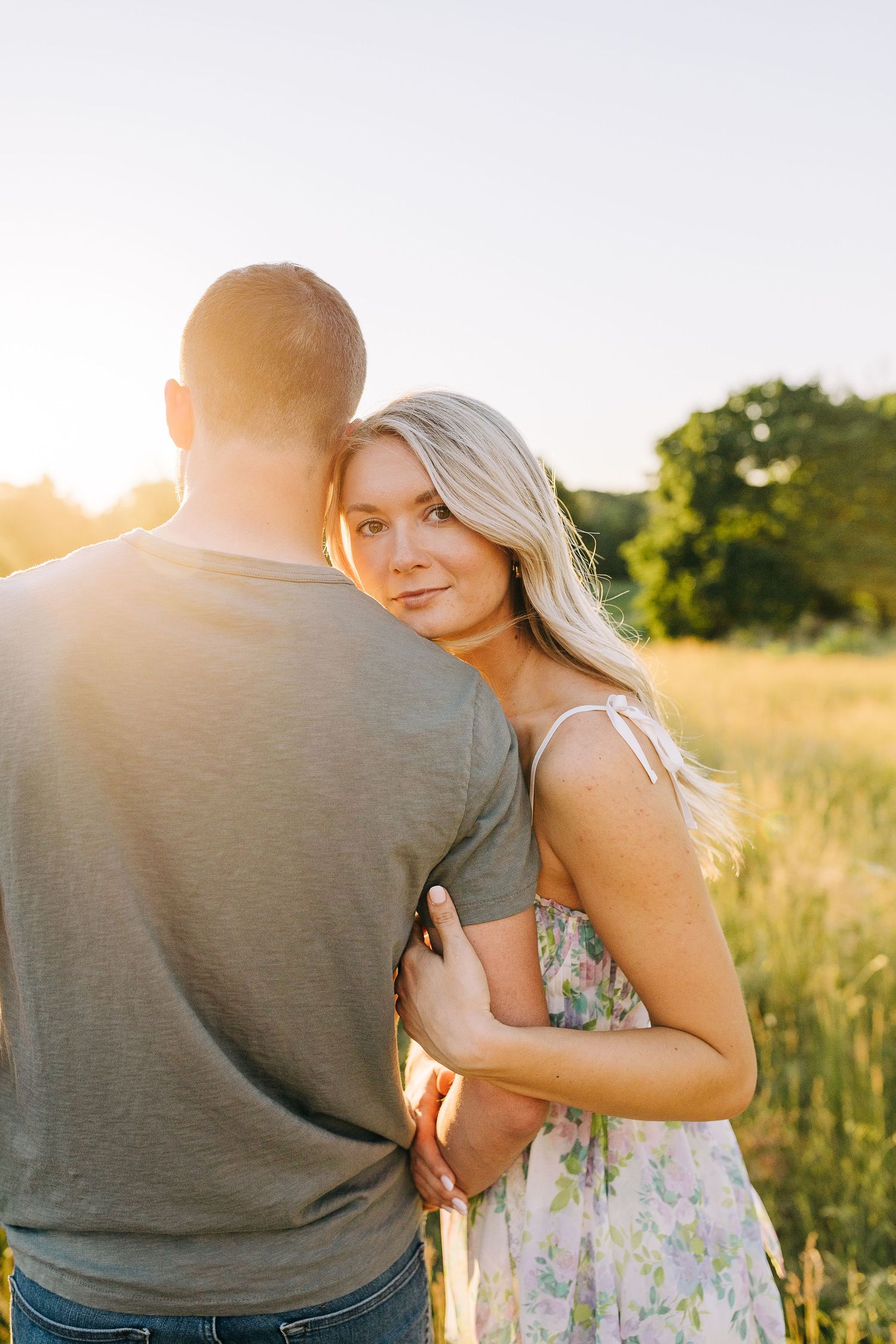 Engaged couple watching the sunset and nature around them in a open field at sunset.