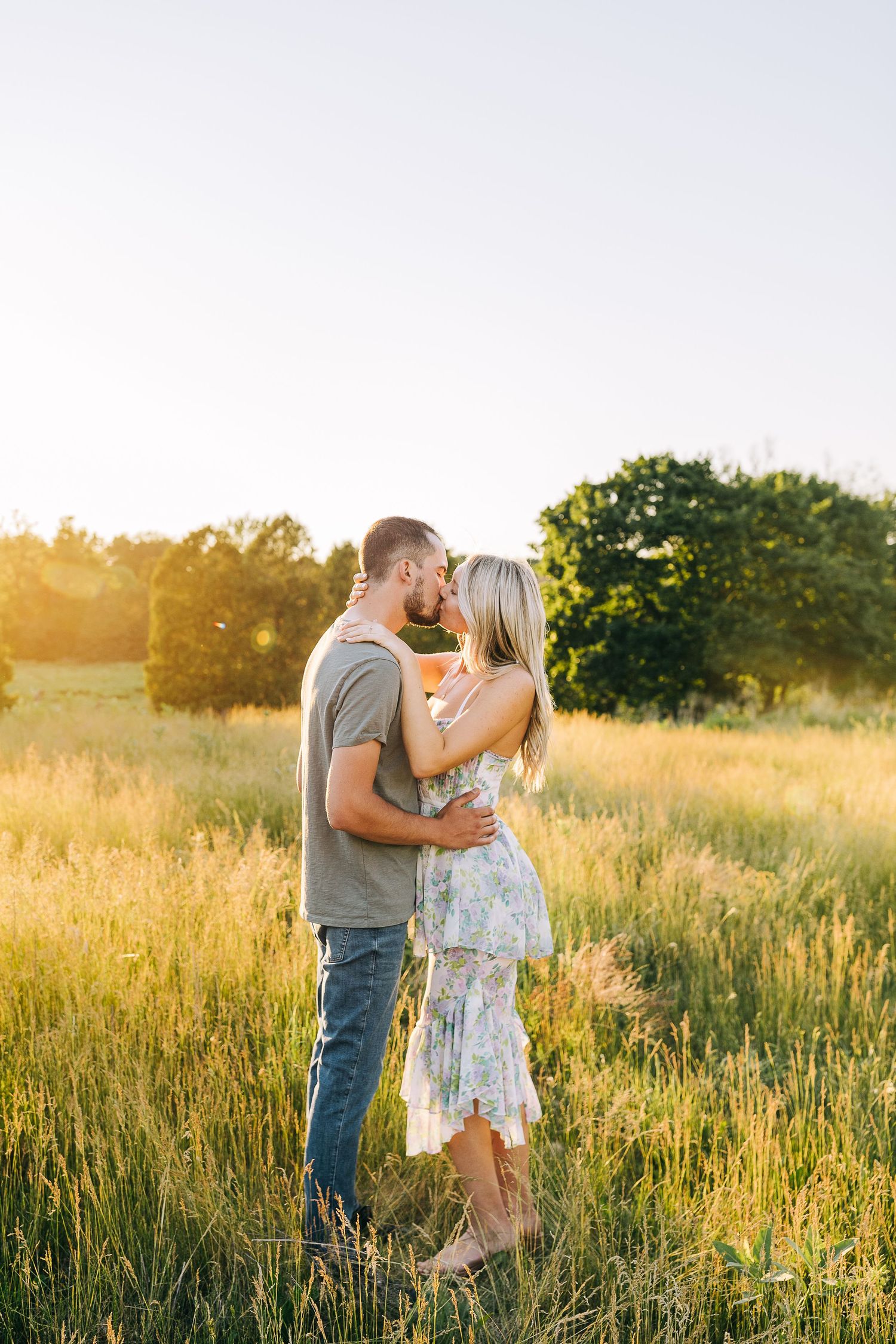 Engaged couple sharing a kiss in a open field of wildflowers at sunset.