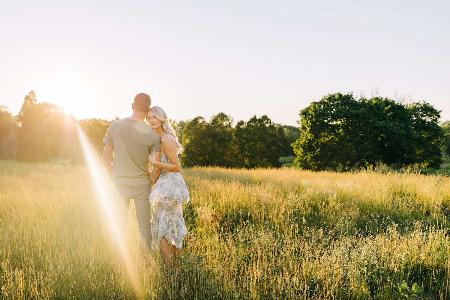 Engaged couple watching the sunset and nature around them in a open field at sunset.