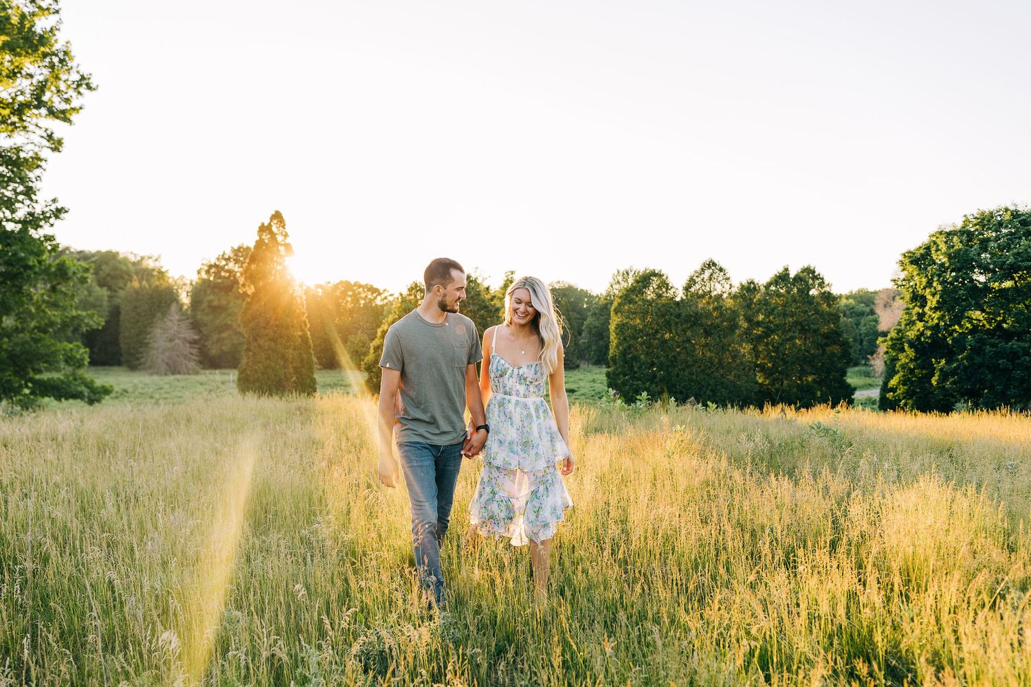 Engaged couple walking hand in hand during sunset in a wide open field.