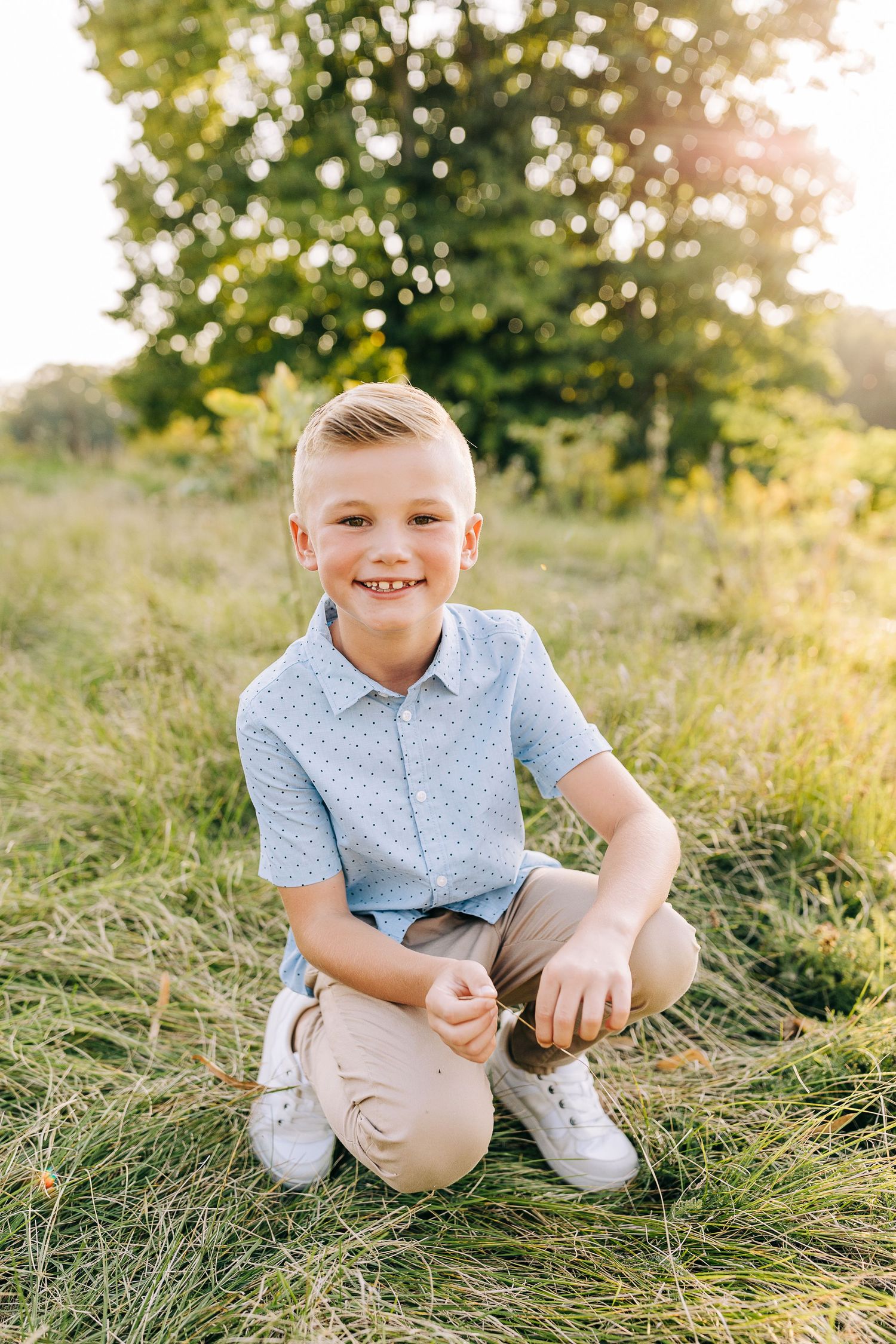Young boy kneeling in grassy field at sunset in the summertime.