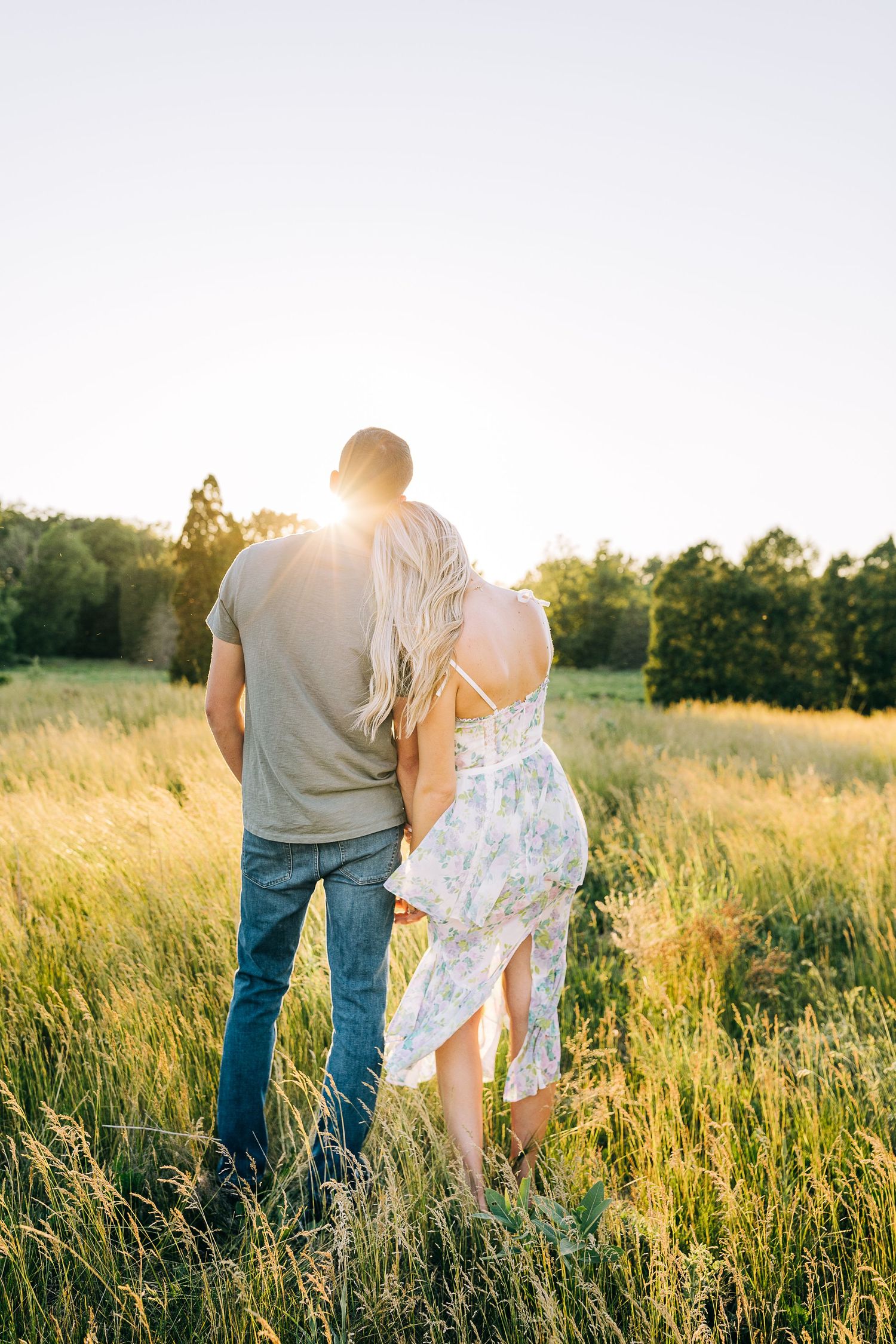 Engaged couple sharing a quiet moment and embrace at sunset in a wide open field with wild flowers.