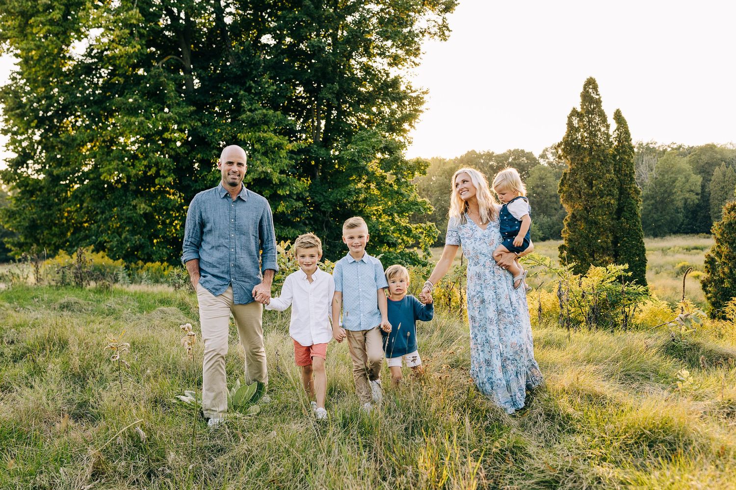 Family, walking through a grassy field at sunset.