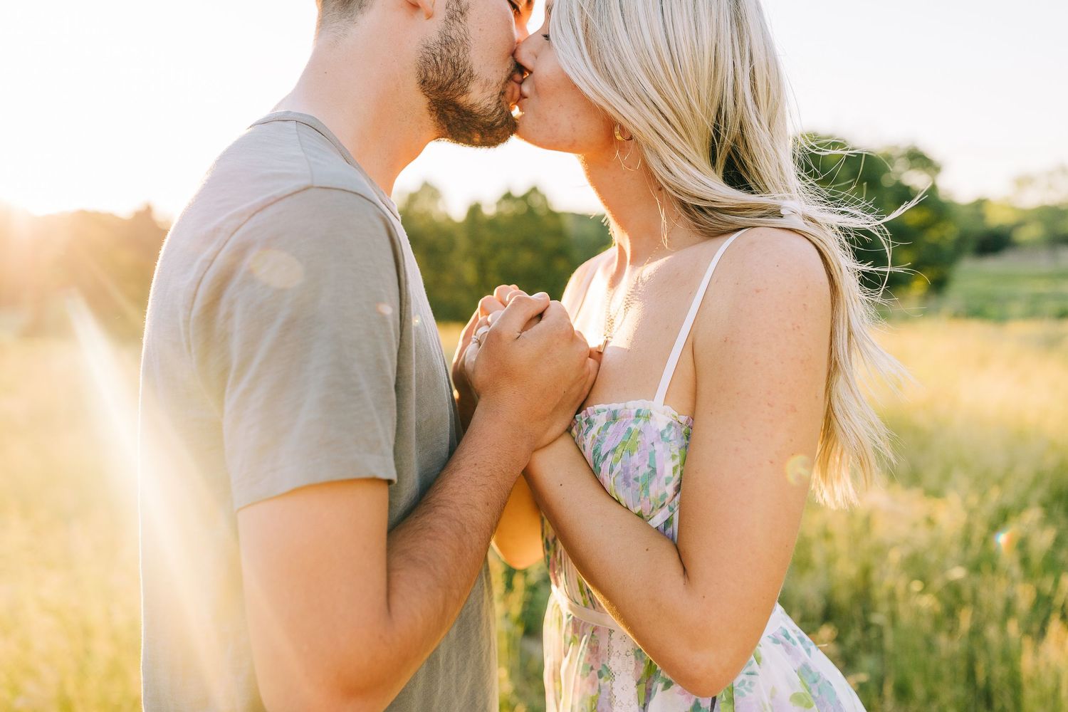 Engaged couple sharing a kiss at sunset in a wide open field.