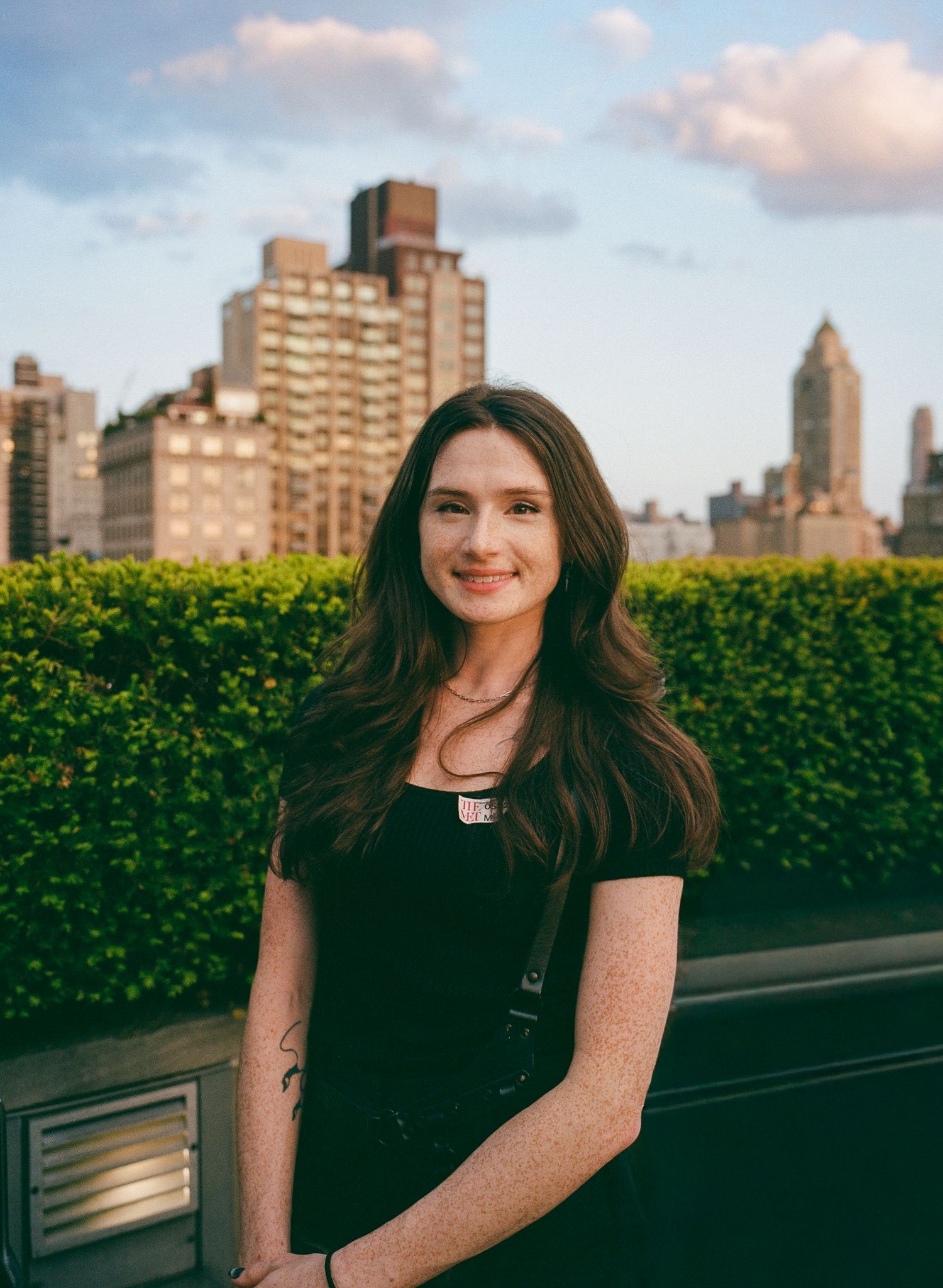 Fine art portrait of a white woman with wavy brown hair captured in front of a cityscape in medium format film photography style.