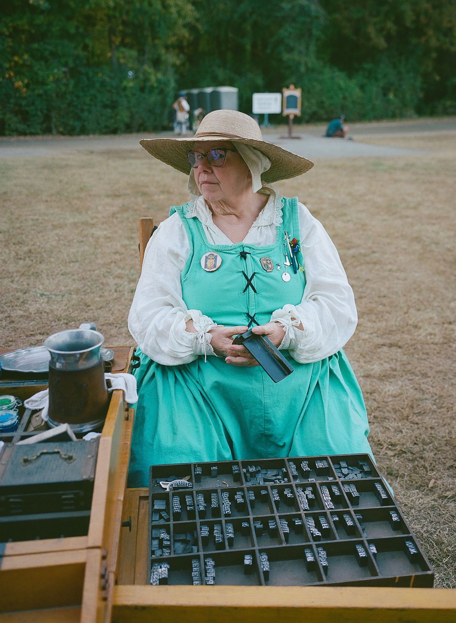 Fine art environmental portrait of a white woman in a teal dress, and white long-sleeved shirt, a wide-brimmed hat, and glasses.
