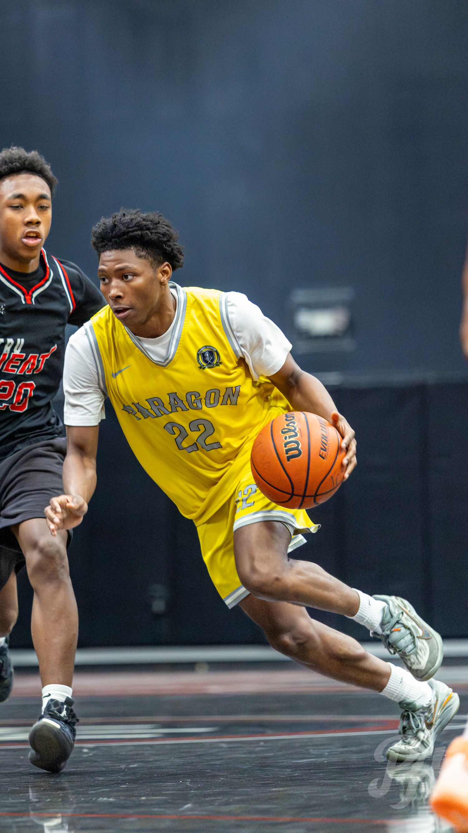 Paragon #22 player drives to basket past defender in yellow jersey during basketball game.