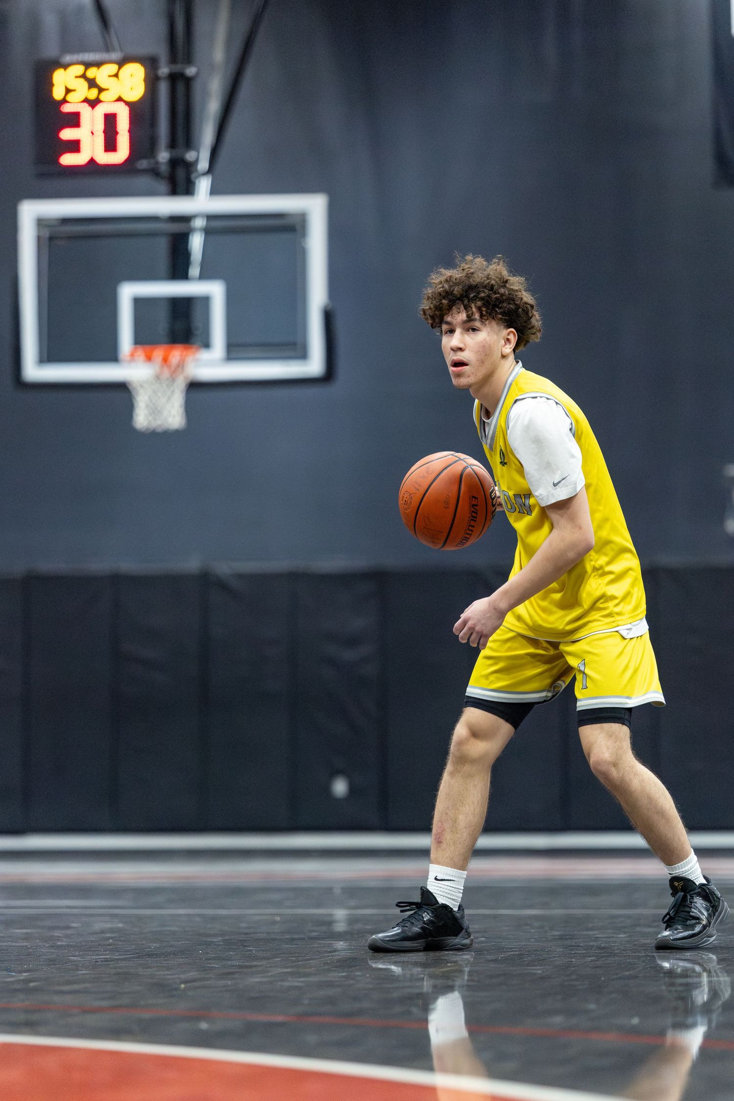 Young basketball player in yellow jersey dribbling ball on indoor court during game.