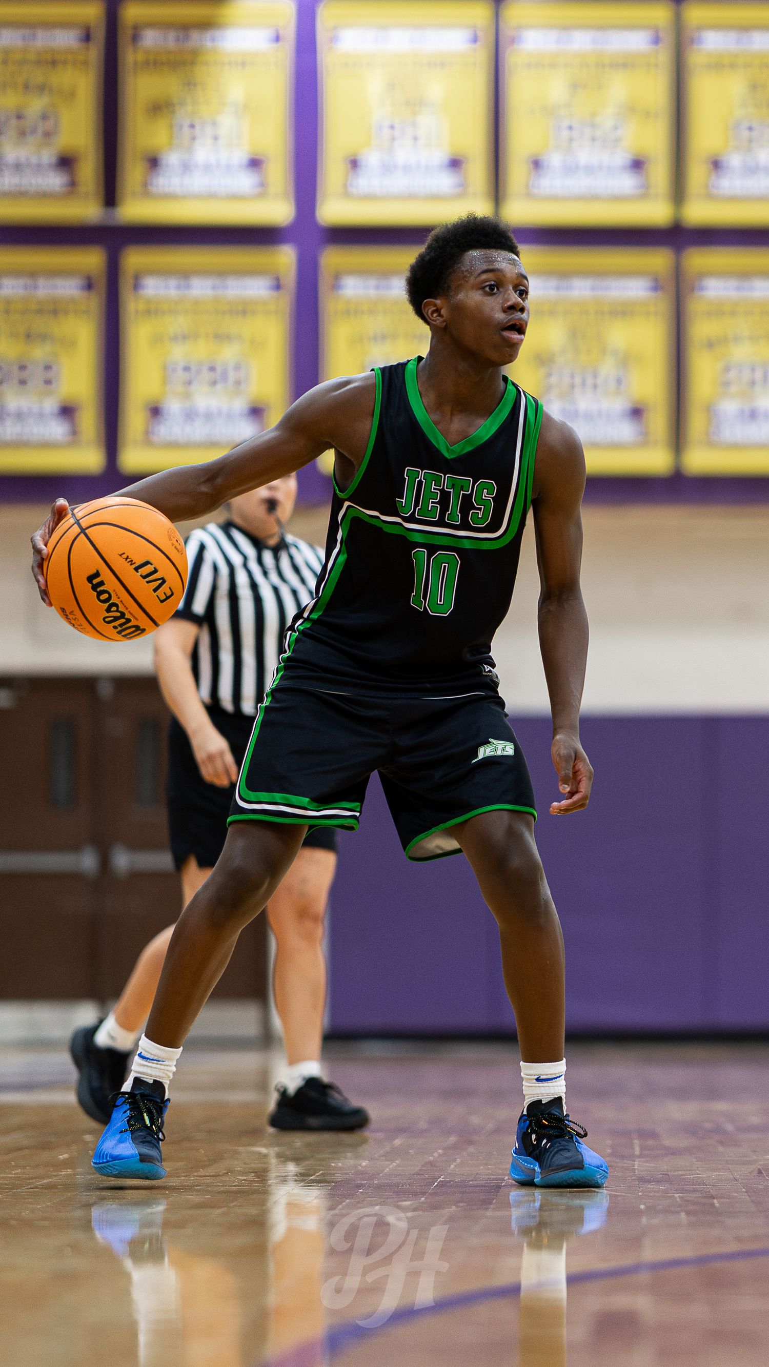 Teen basketball player #10 in Jets black uniform dribbles ball during high school gymnasium game.