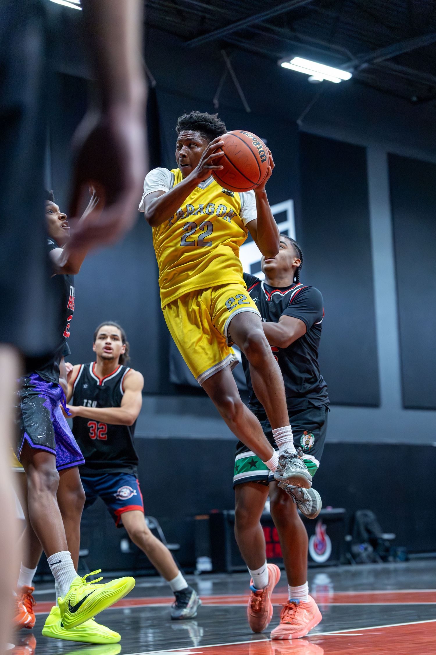 Paragon basketball player #22 in yellow jersey grabs rebound during competitive indoor game.