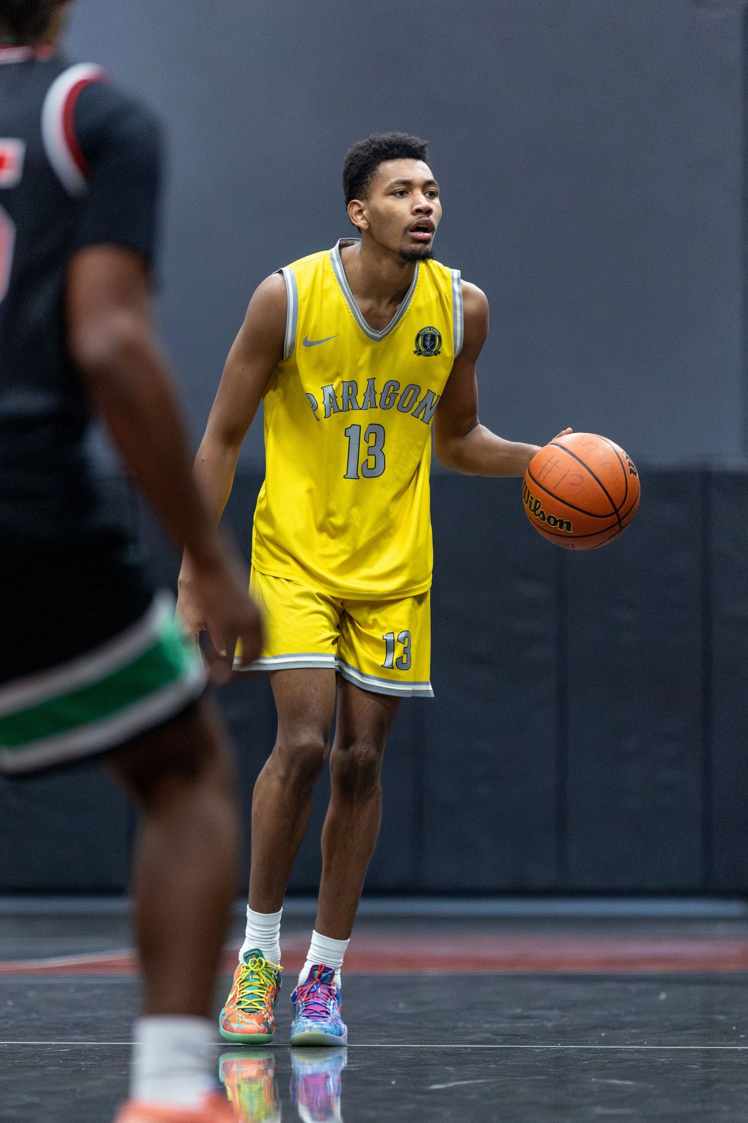 Basketball player #13 in yellow Paragon jersey dribbling during indoor game.
