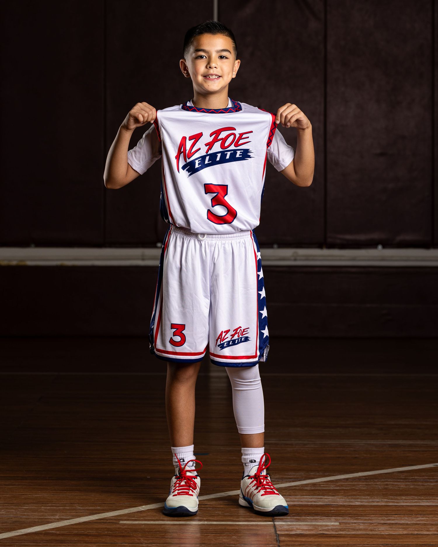 Smiling young basketball player #3 proudly displays AZ Foe Elite jersey in professional studio portrait.
