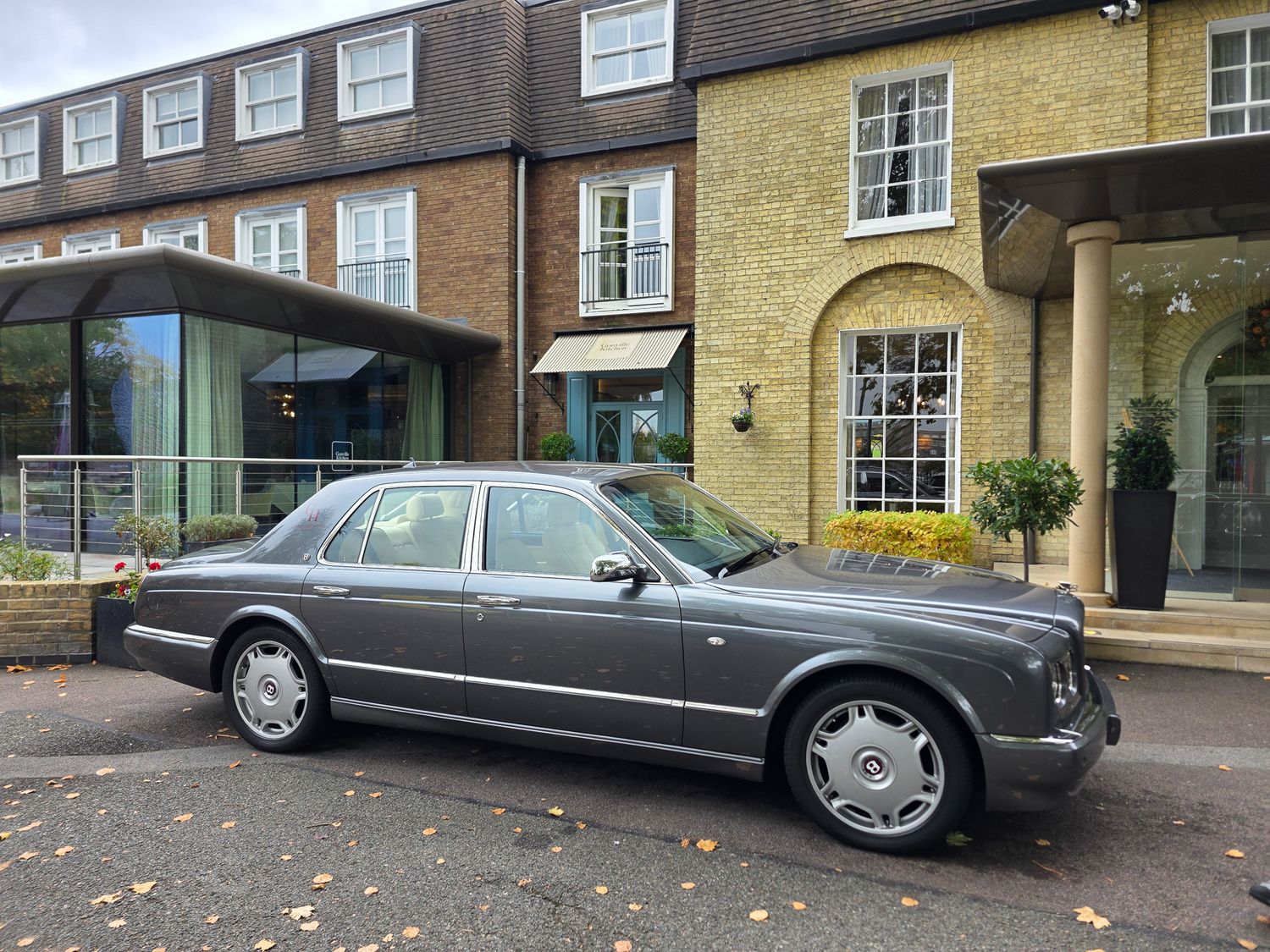 A long gray luxury Bentley limousine parked in front of a brick building.