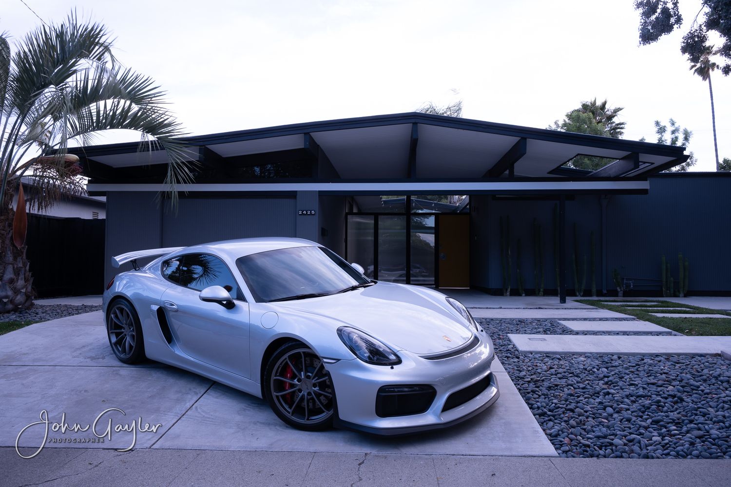 A monochrome portrait of a Porsche Carrera GT4 rests outside a modern Eichler designed house