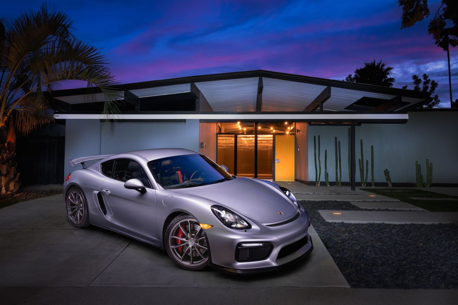 A silver Porsche 981 Cayman track-oriented GT4 light painted on the driveway of a Joseph Eichler designed home in the San Francisco Bay Area