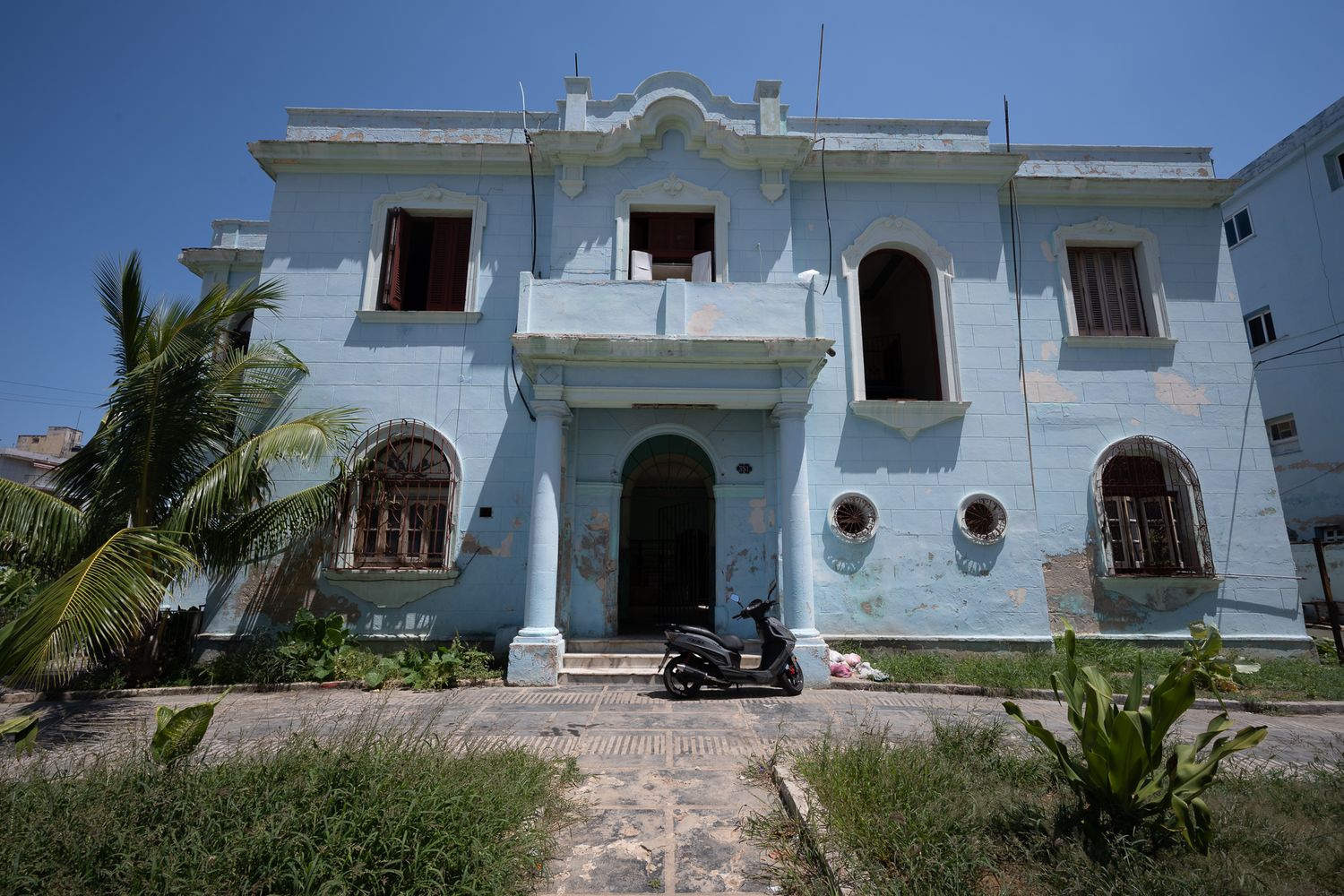Light blue colonial mansion with arched windows and palm trees in front features vintage architecture in tropical setting, Old Havana, Cuba