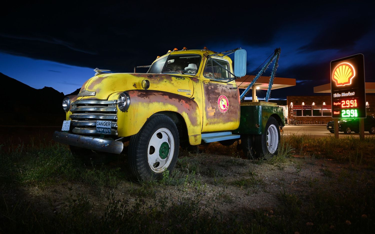 John Gayler light painting of a rusted classic Chevrolet work truck outside a modern gas station in Colorado with a skeleton inside