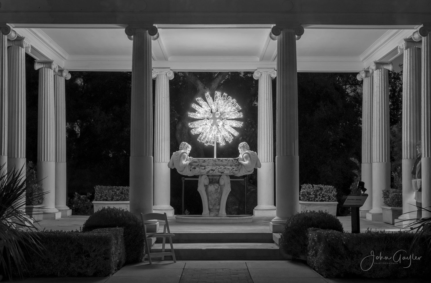 A black and white photograph of a greek temple altar with illuminated starburst cross between classical columns.