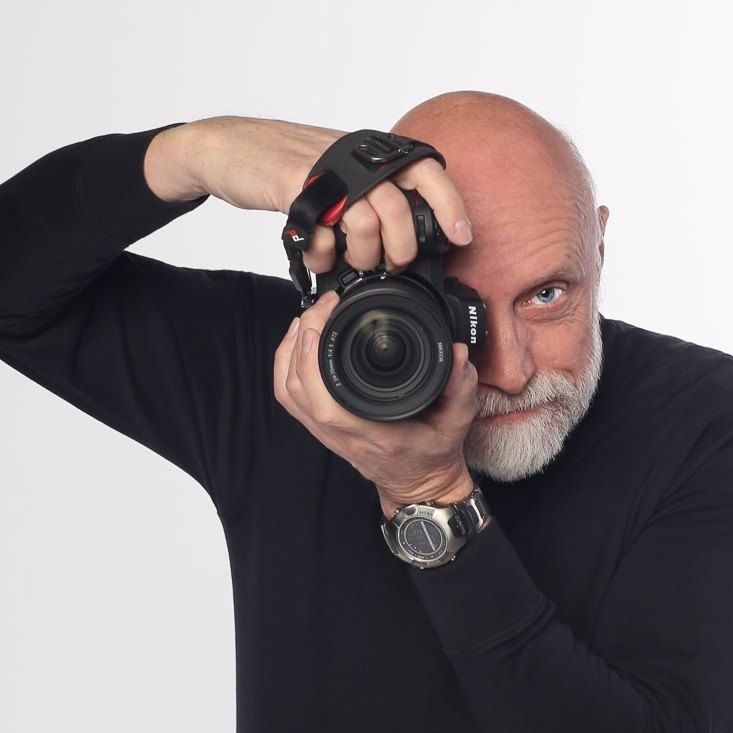 John Gayler is a Master Photographer and member of the Professional Photographers of America. Shown holding his camera  looking intently.