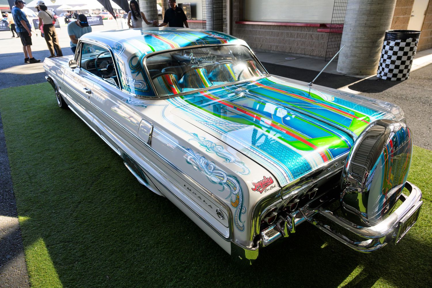A classic lowrider car with chrome details and custom paint job displayed at an outdoor event.