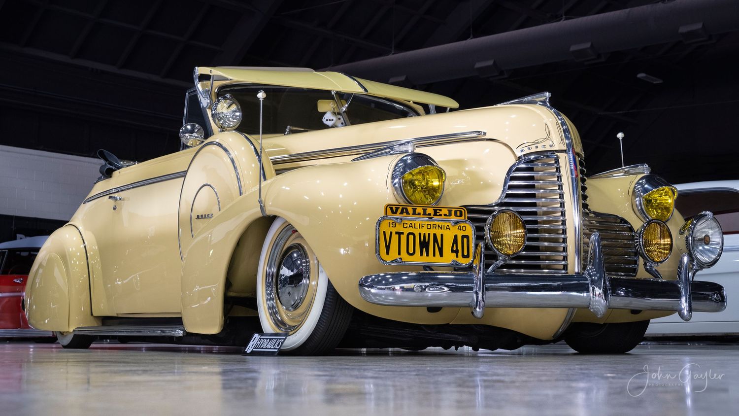 Vintage cream-colored 1940 Buick Special convertible with custom lowered suspension and whitewall tires on display at an auto show.