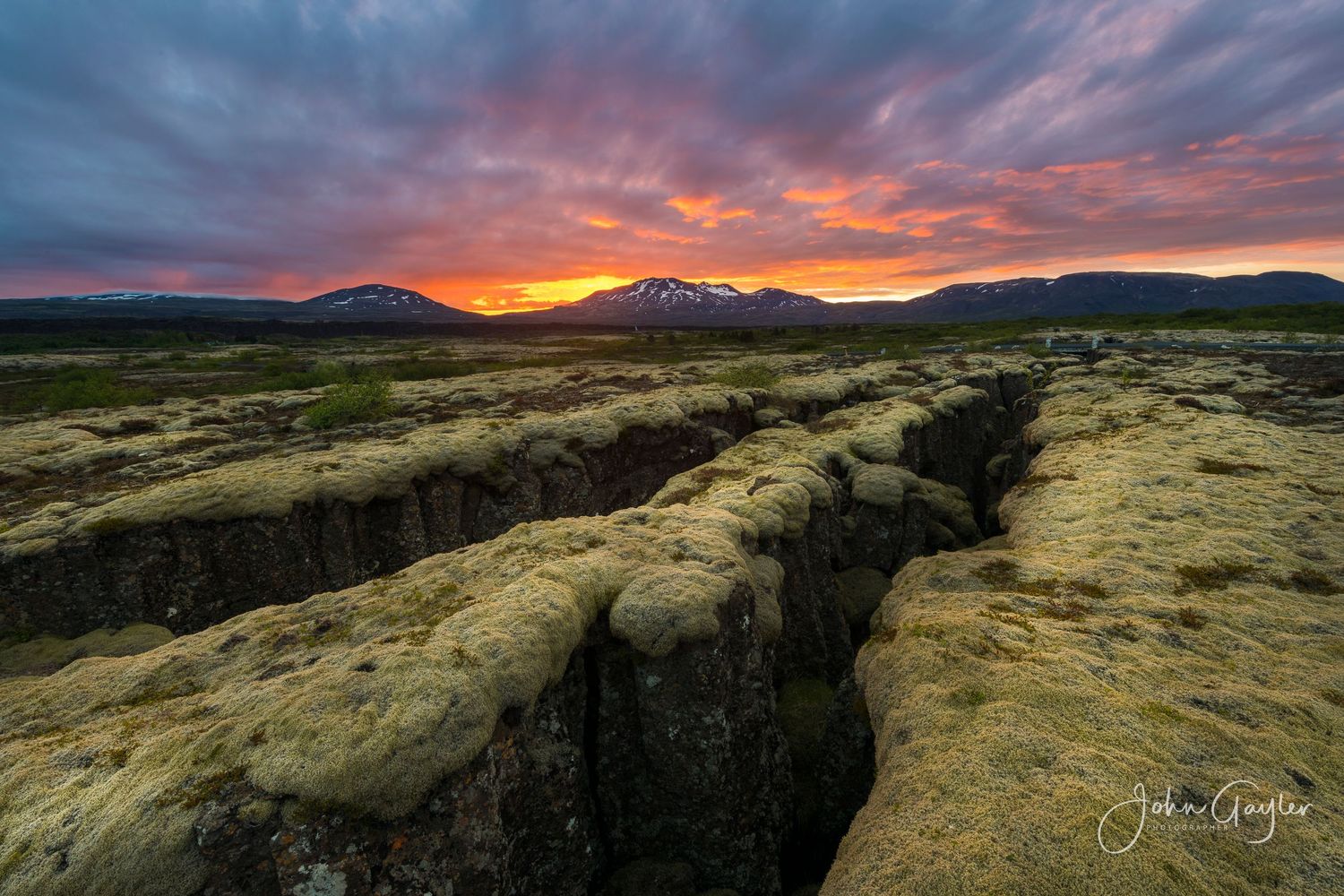 A dramatic panoramic view of lava and rolling hills at sunset with vibrant orange and purple clouds in an Icelandic sunset.