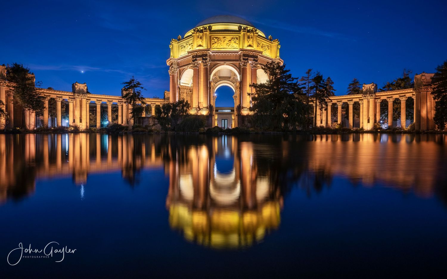 Palace of Fine Arts illuminated at night with golden lights reflecting in the lagoon in San Francisco, California.