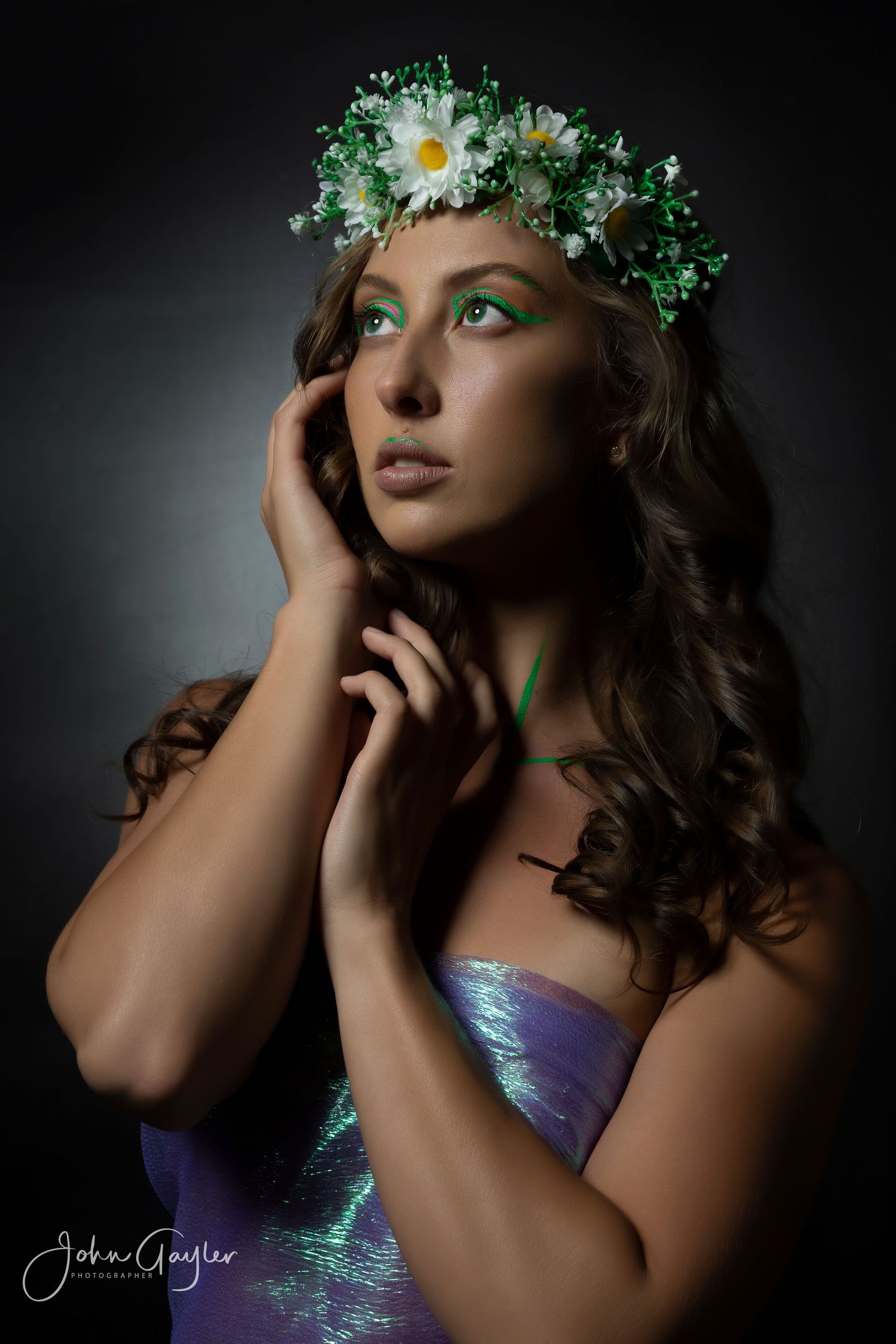 Artistic portrait with floral crown featuring white daisies and green accents against dramatic dark backdrop.