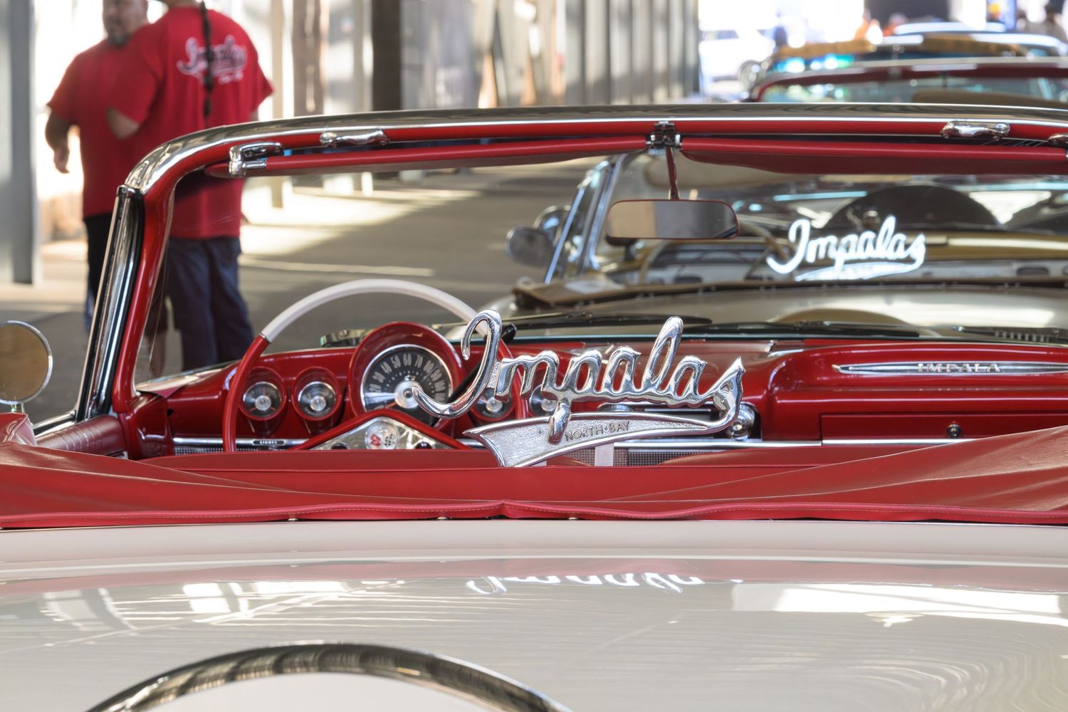 A classic Chevrolet Impala with glossy white paint and a red interior has a chrome sign for the Impala Low Rider club