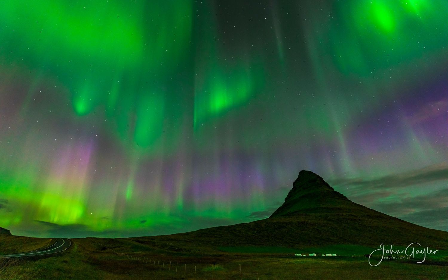 Vibrant green aurora borealis dances across the night sky over dark mountain silhouettes of  kirkjufell in west Iceland.