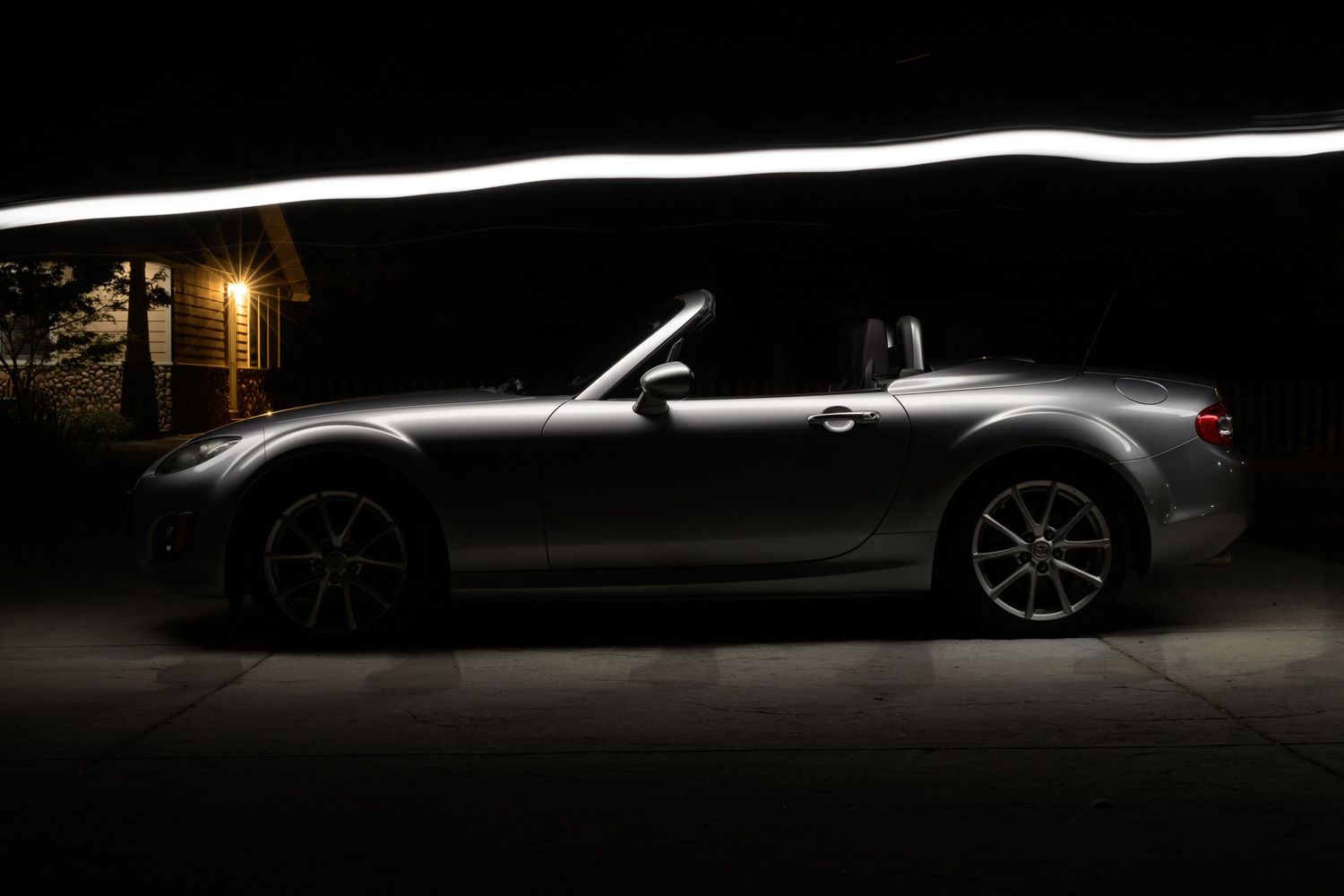 A silver Mazda Miata MX-5 sports car photographed at night with dramatic overhead lighting during a John Gayler light painting session.