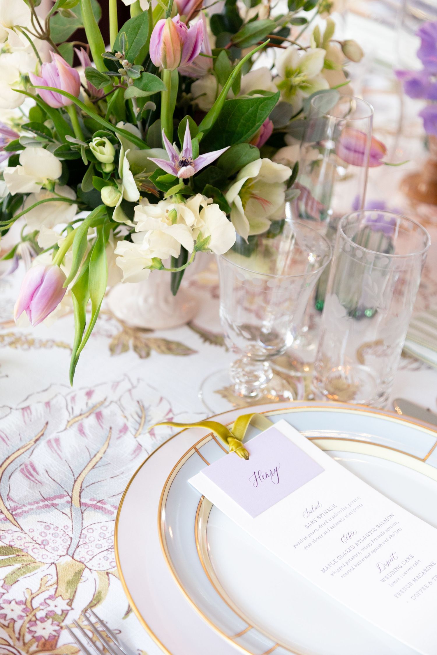 Elegant place setting with gold-rimmed plates and floral centerpieces for wedding reception.
